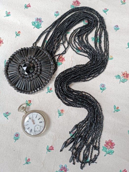 French Brocante - For Sale - Flower Head & Fringe Costume AccessoryDescription: <p>An unusual costume embellishment that appears to have attached to a dress or bodice with press studd, there are three on the back of the large flower head which is made up of a large faceted central bead, baguette beads and circles of smaller faceted jet beads, 5 of the long strands are tipped with teardrop beads the others are missing.</p>

<p>Flower head is 10cm diameter, the strands hang down 56cm</p>
